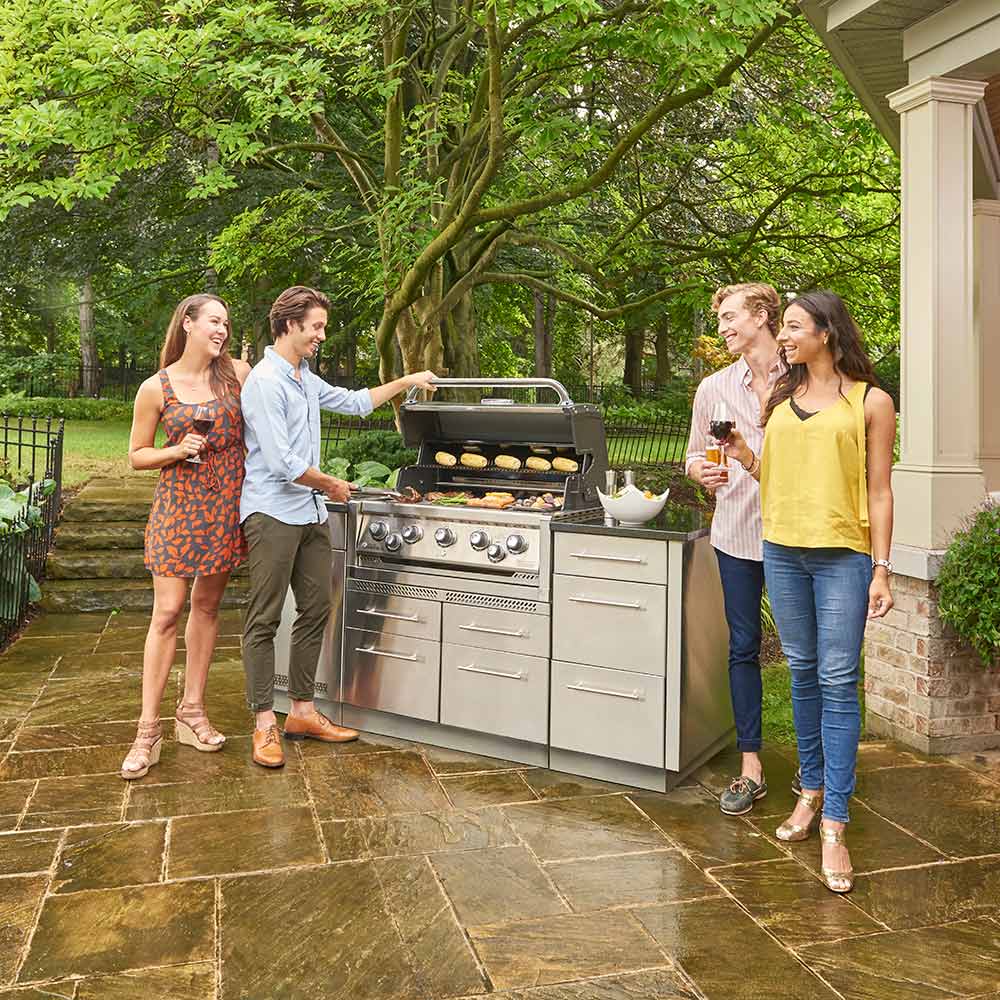 Stainless steel gas grill on outdoor patio with people standing nearby