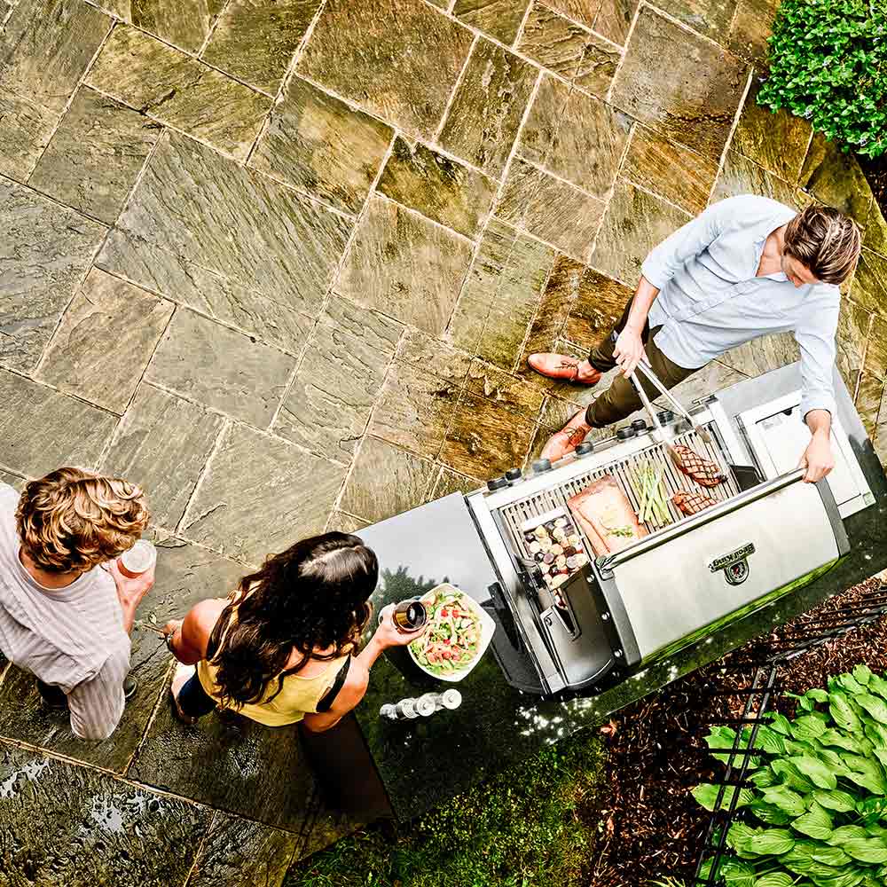 Stainless steel gas grill with open hood, shown from above on outdoor patio