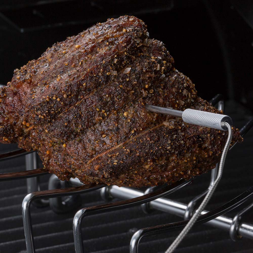 Smoked meat with seasoning on grill grates and metal thermometer probe