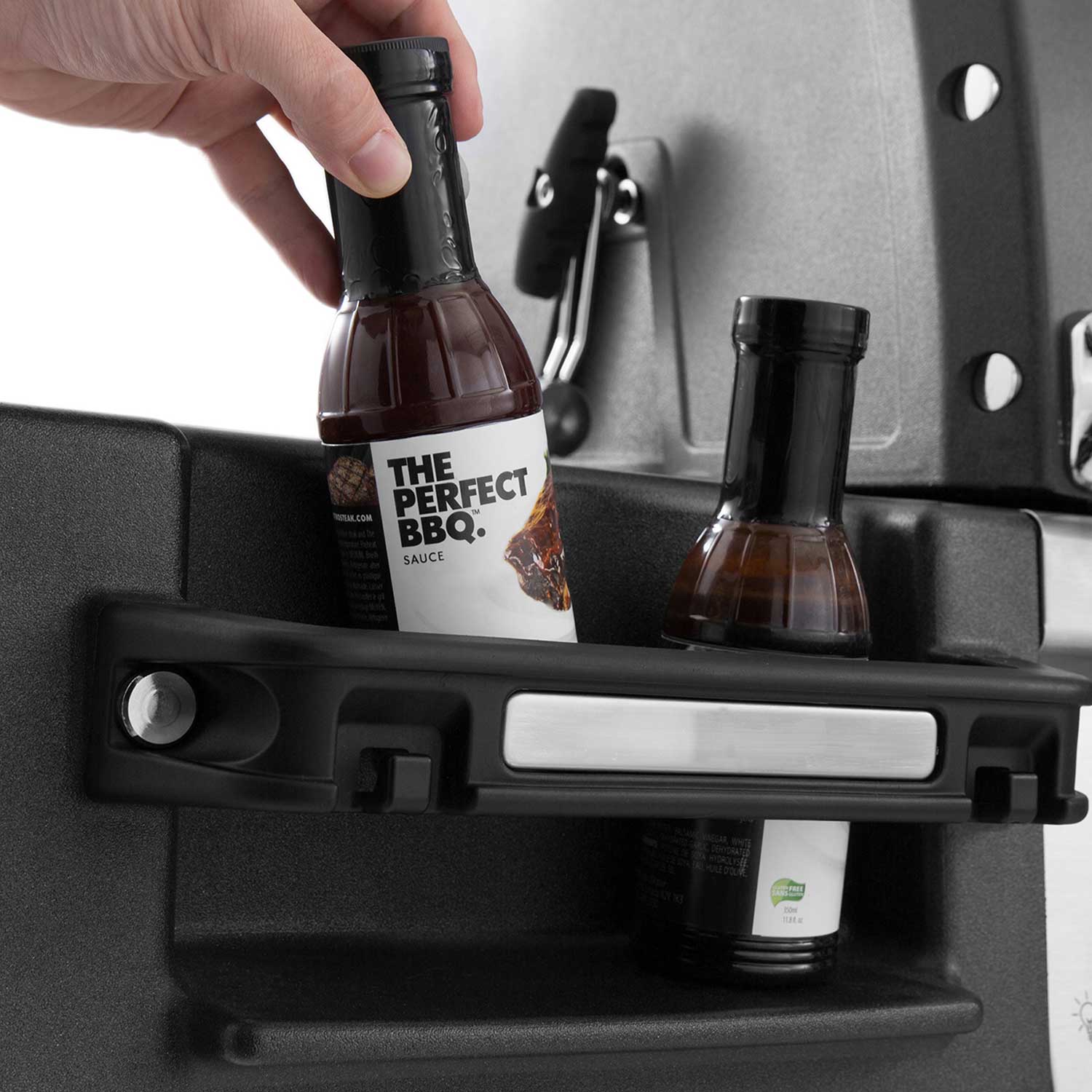 Gas grill side shelf with BBQ sauce bottles and sauce display, close-up.