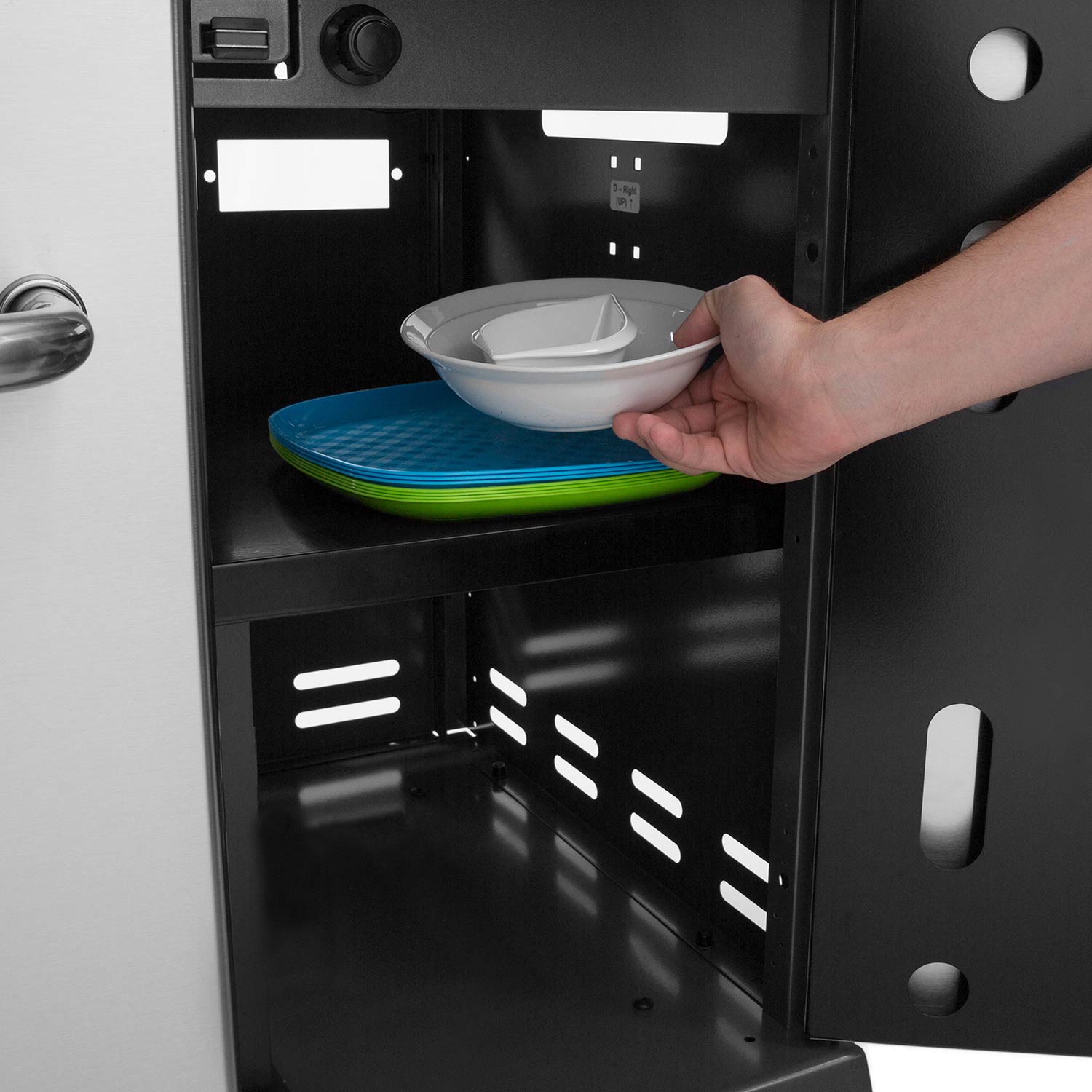 Gas grill lower storage compartment with shelf racks and hand placing a bowl, close-up.