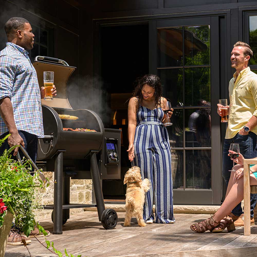 Black pellet smoker and grill with smoke and open cooking hood on patio