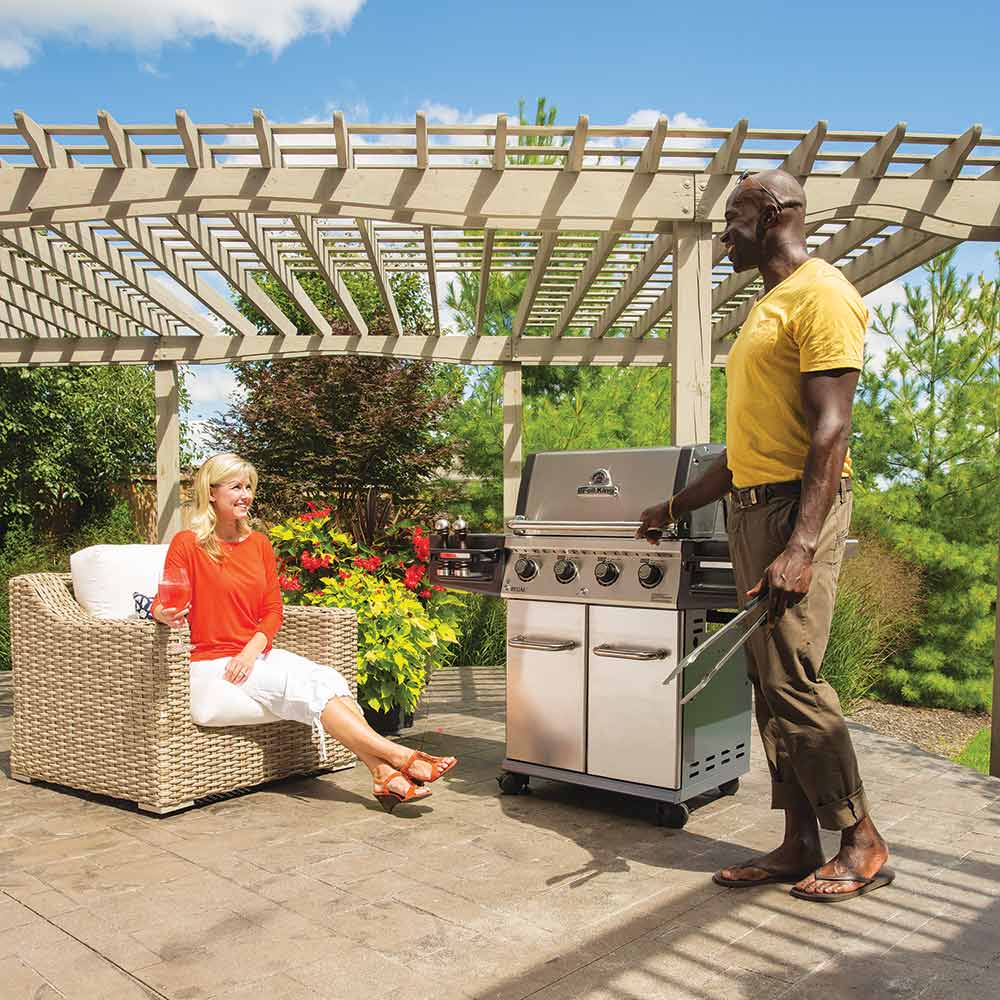 Freestanding gas grill on wheeled cart, stainless steel body with two cabinet doors and knobs.