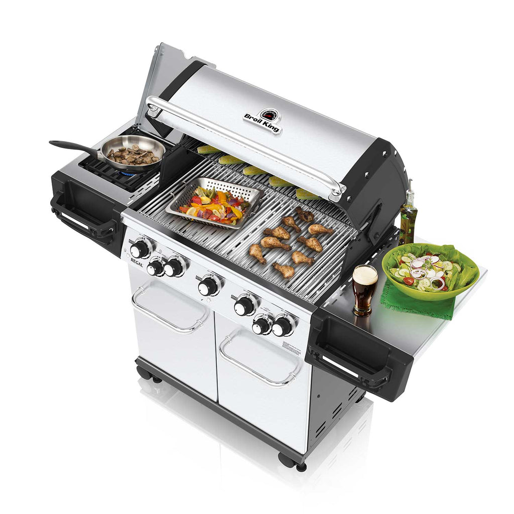 Open gas grill with food on grates and side shelf, stainless cooking chamber