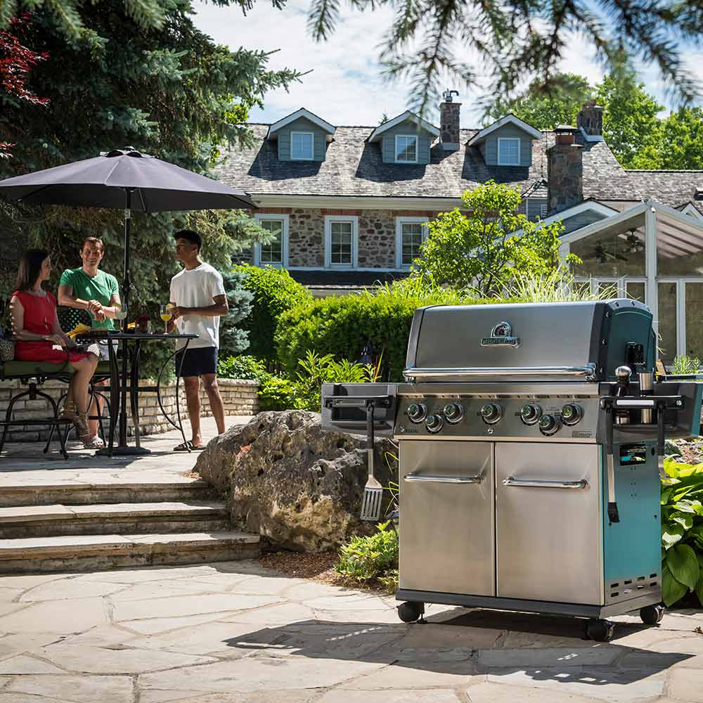 Freestanding stainless gas grill on stone patio with control panel and side shelf