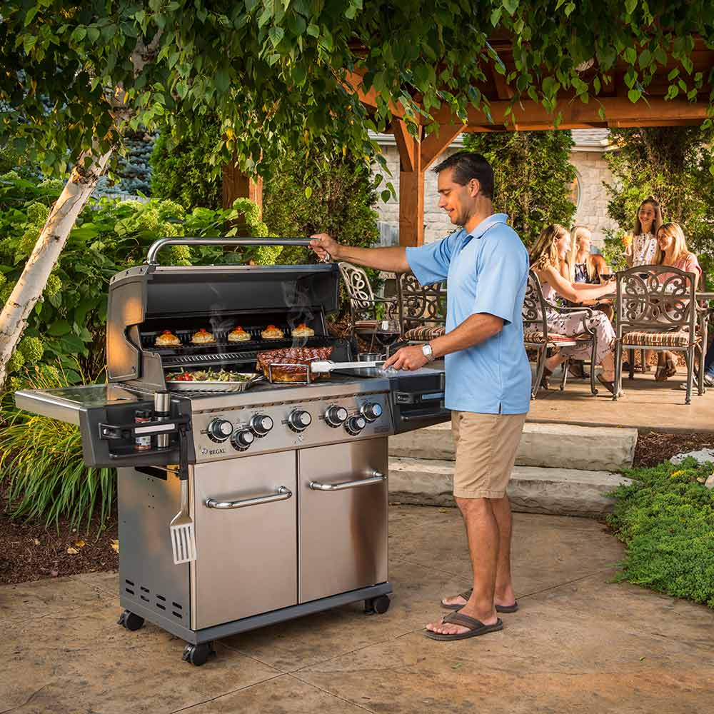 Stainless gas grill on patio with man grilling, side cabinet doors and knobs visible