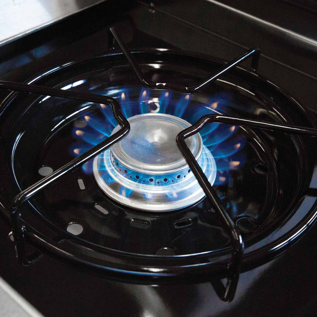 Gas grill burner head with blue flame around the center, viewed from above