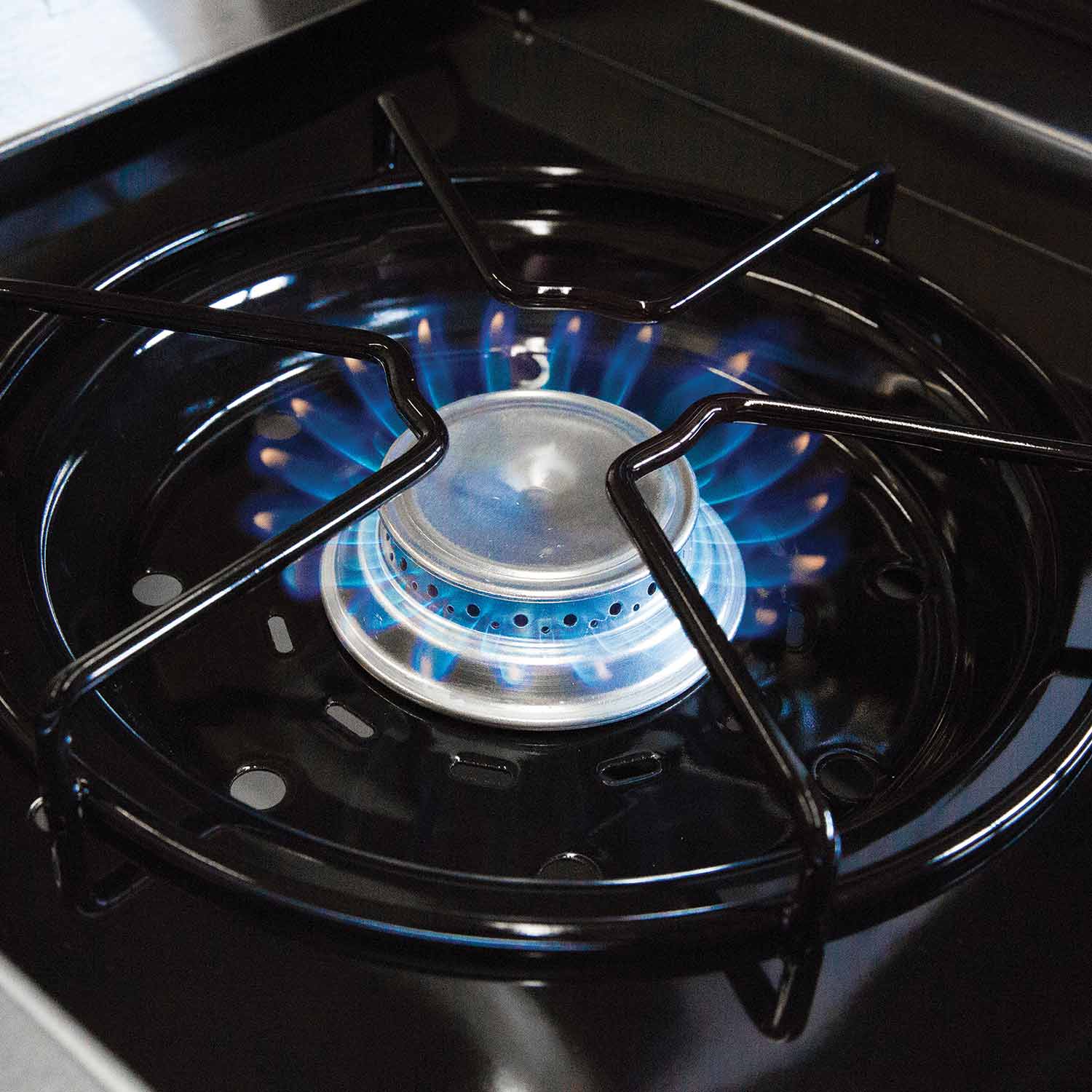 Gas grill burner head with blue flame around the center, viewed from above