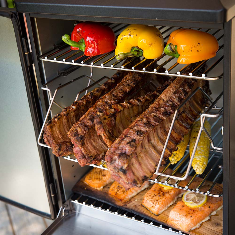 Smoker interior with ribs and vegetables on wire racks, with door open