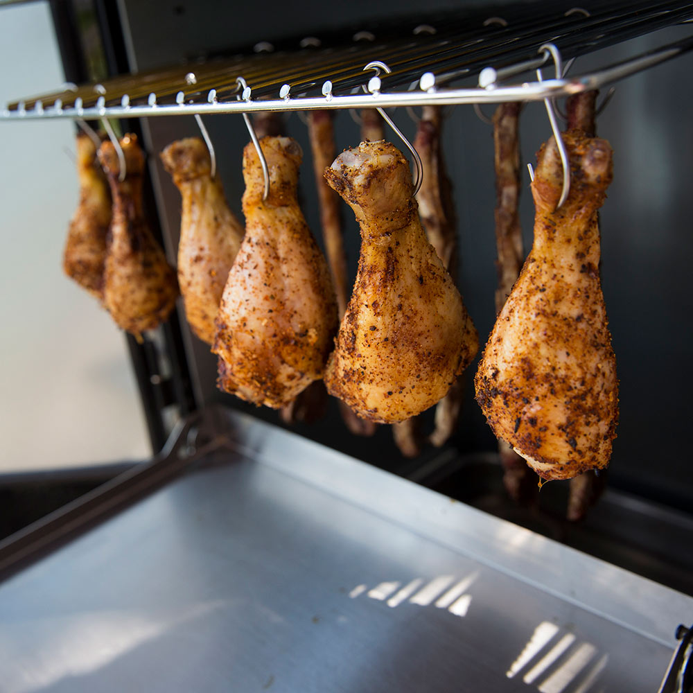 Smoker cooking rack with hanging seasoned poultry pieces, door open