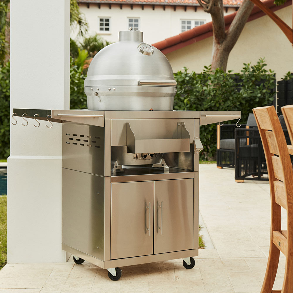 Kamado grill on cart outdoors with closed dome and cabinet storage doors