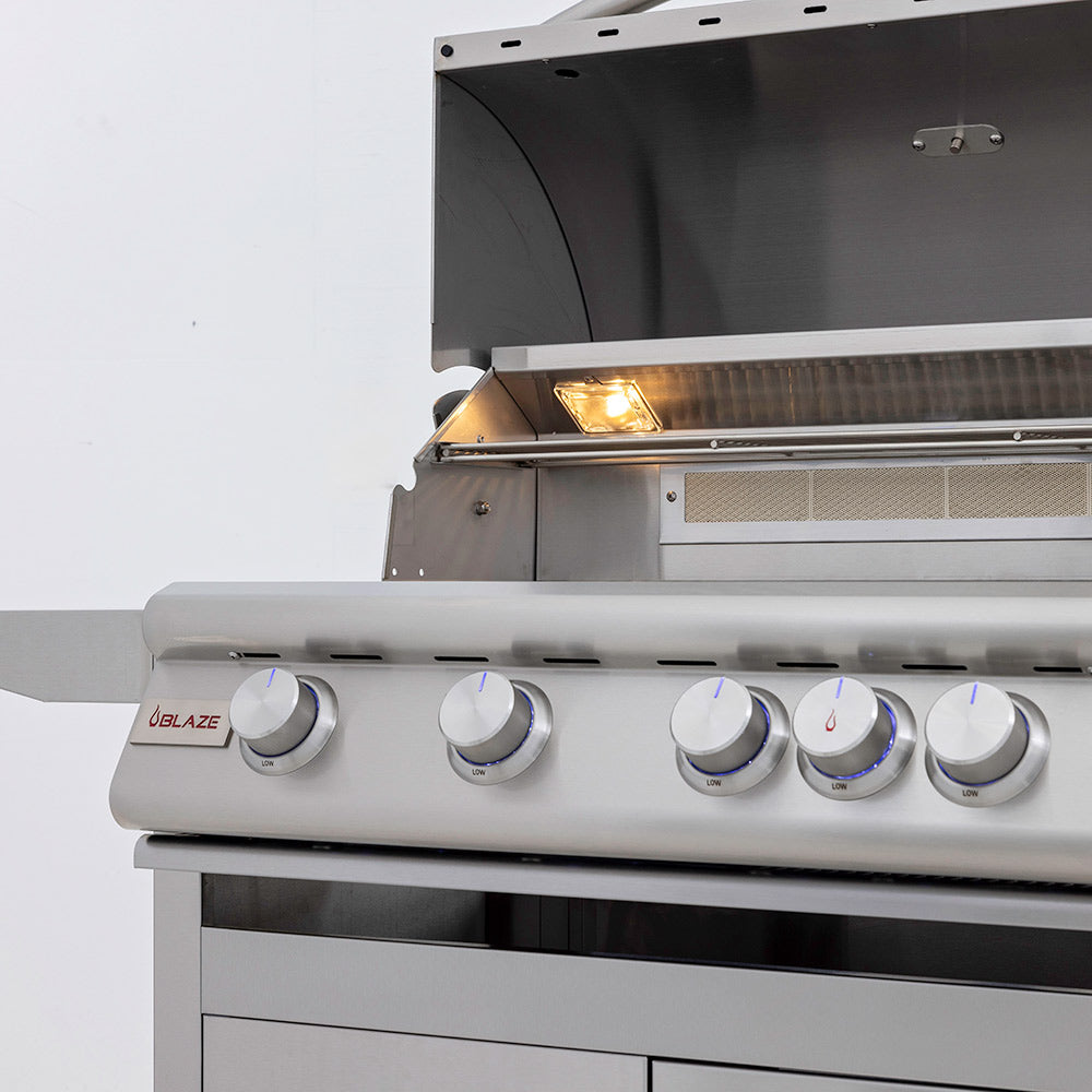 Gas grill open lid showing lit burner area and control knobs, close-up