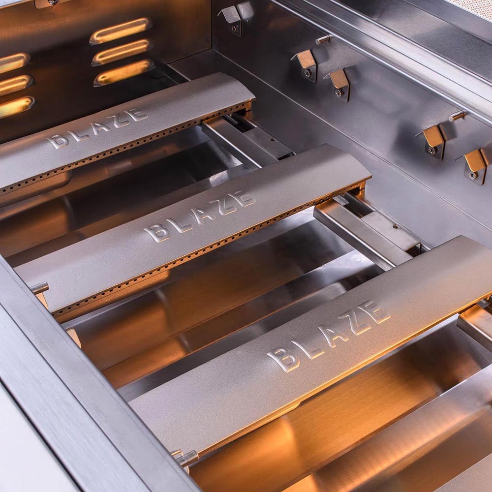 Gas grill firebox with Blaze GRILLS branding on heat shields and burner tubes