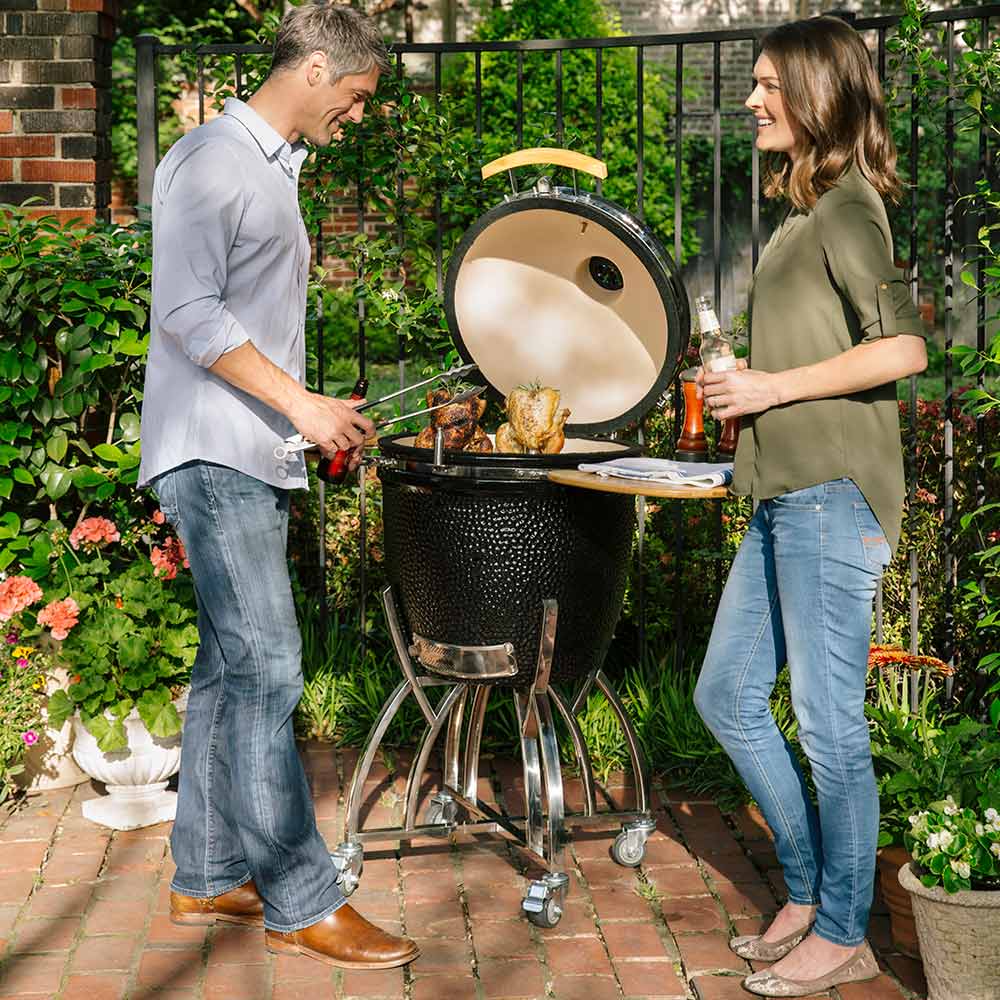 Outdoor ceramic smoker grill with open lid, wooden side shelves, and wheeled base
