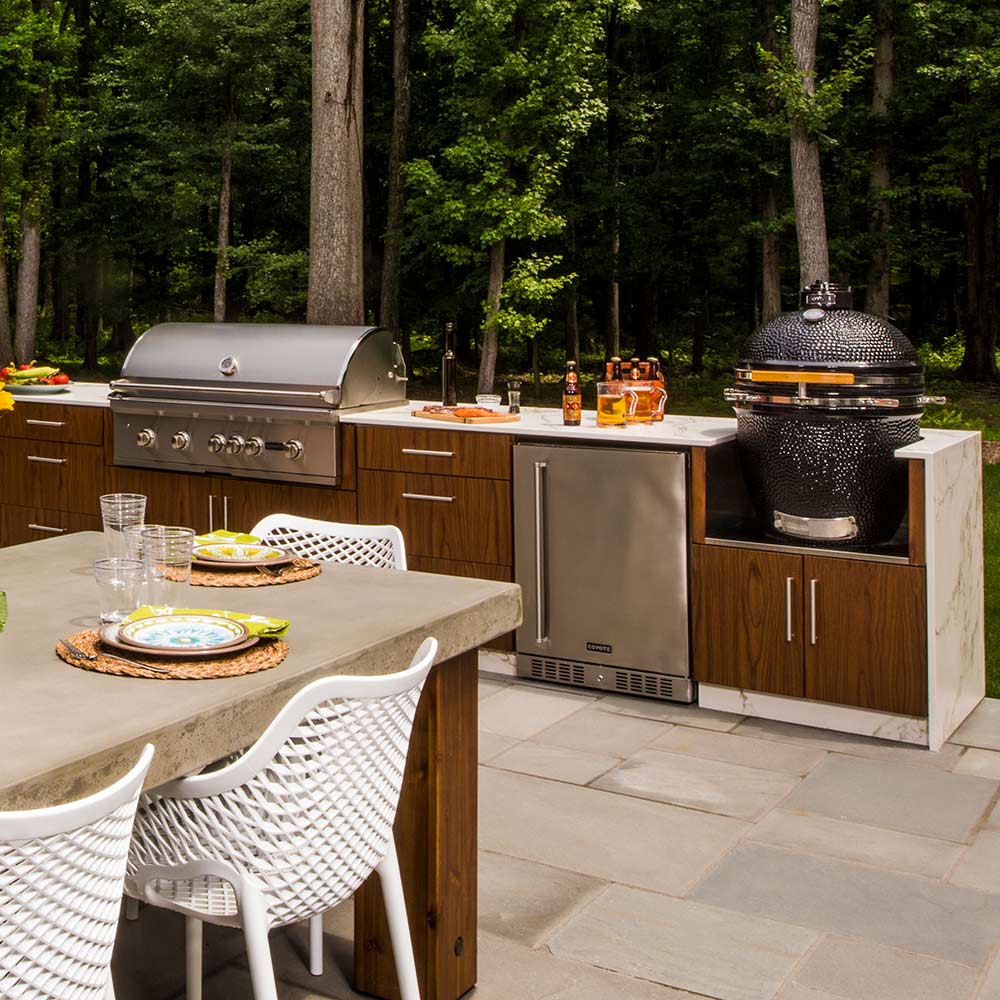 Outdoor kitchen setup featuring built-in ceramic asado smoker with black dome and open cooking