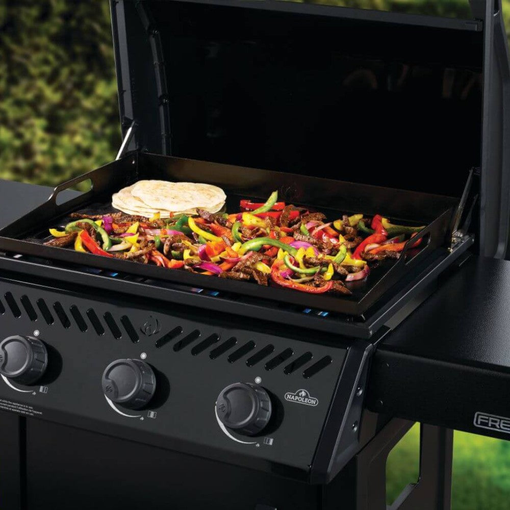 Gas griddle with vegetables, peppers, and meat cooking on the flat griddle surface