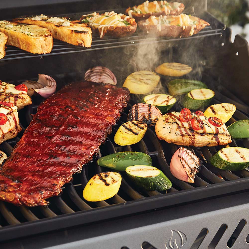 Gas grill cooking surface with meat and sliced vegetables on the grates