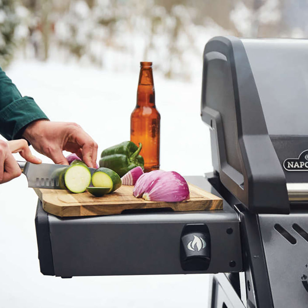 Gas grill on cart with side shelf holding sliced vegetables and a pepper