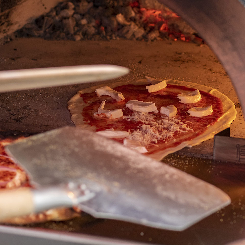 Aluminum pizza peel sliding under a topped pizza in a brick-style oven