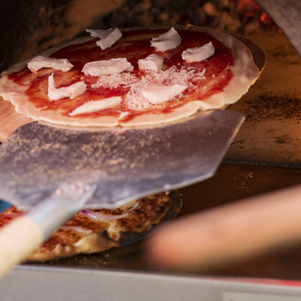 Aluminum pizza peel lifting a topped pizza for transferring