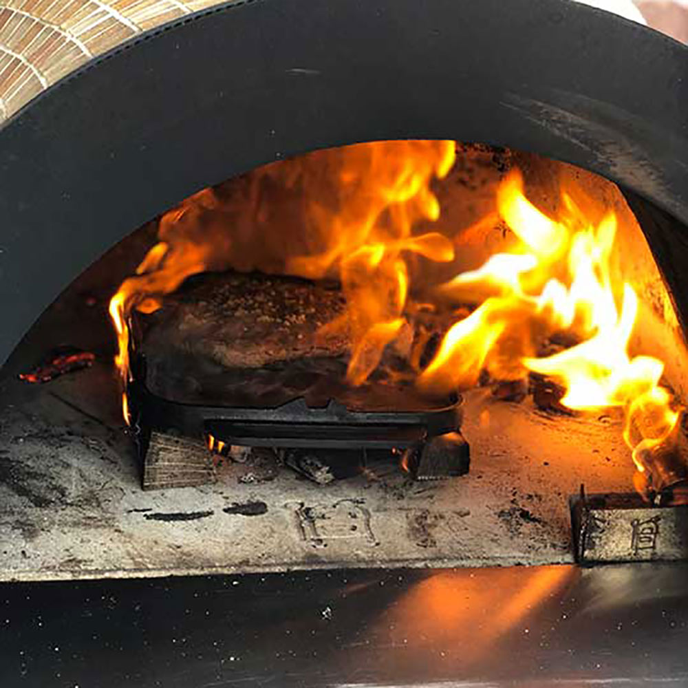 Open fire inside a black pizza oven with stone floor and bright flames