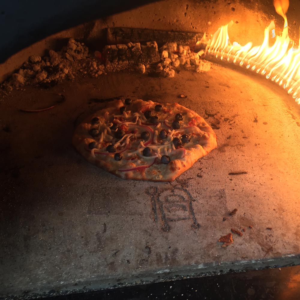Pizza cooking on stone inside a dome oven, flames and heat visible