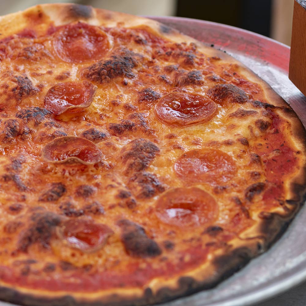 Round aluminum pizza oven pan filled with browned pepperoni pizza