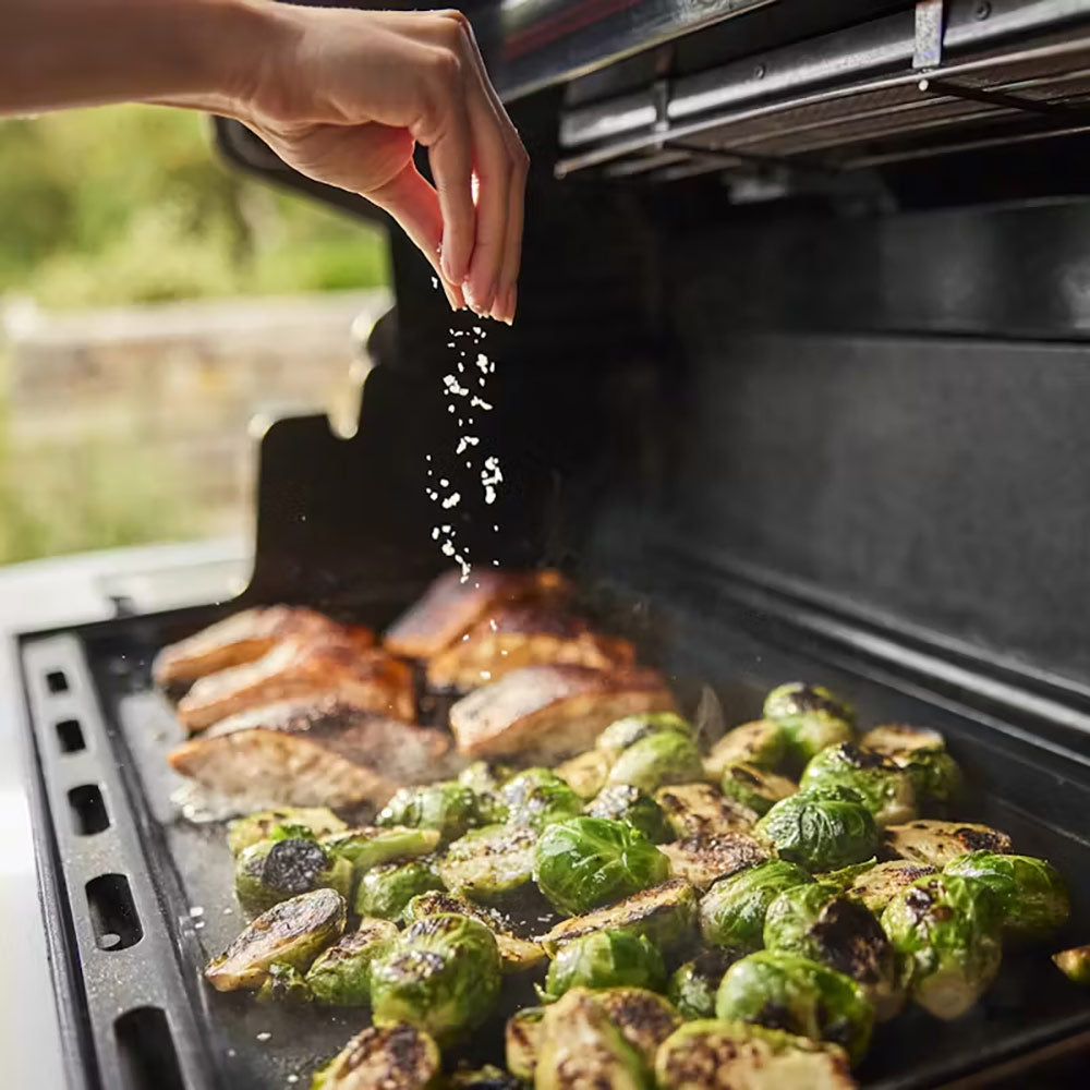 Gas grill with lid open, cooking burgers and Brussels sprouts on the grates