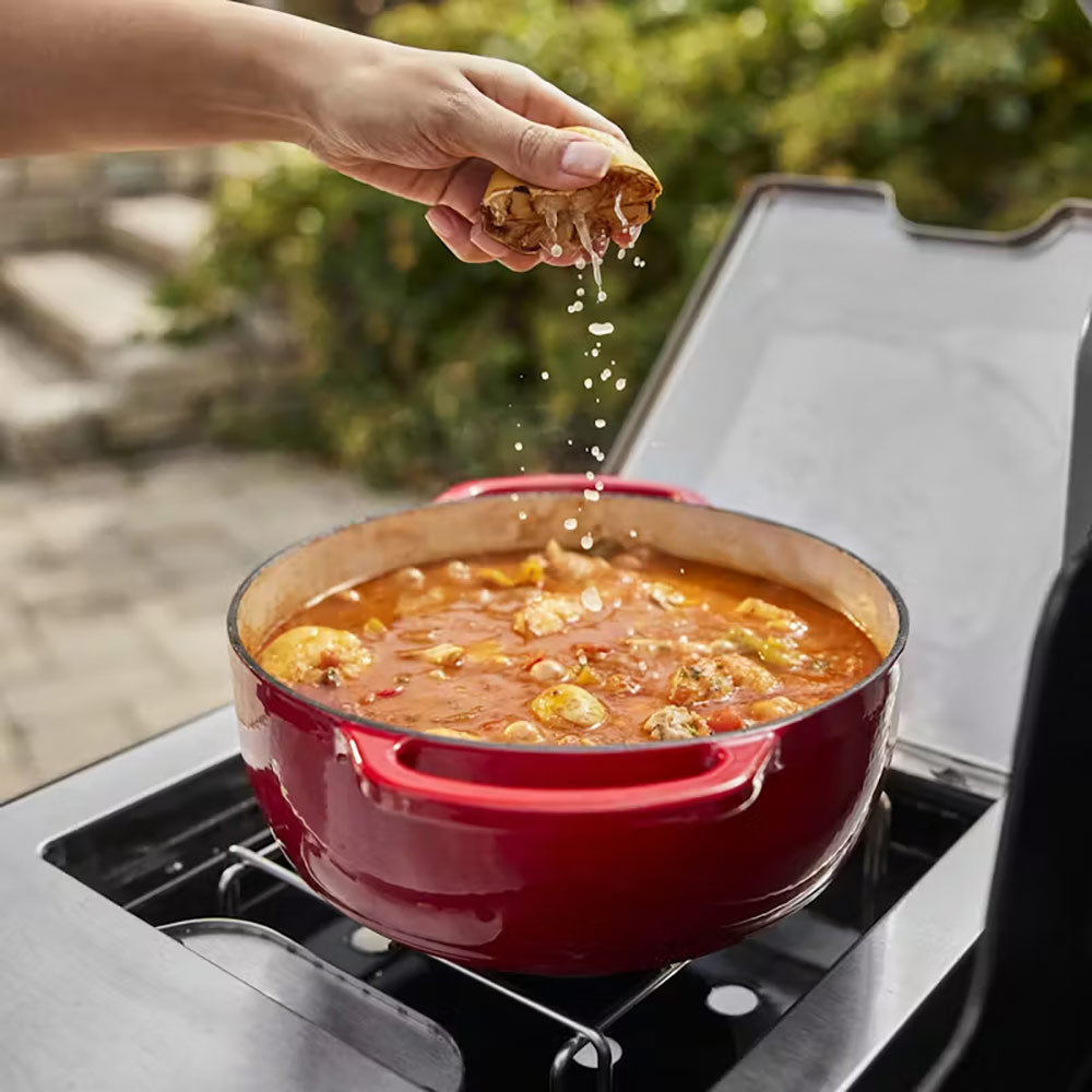 Red pot of food simmering on a gas grill side burner