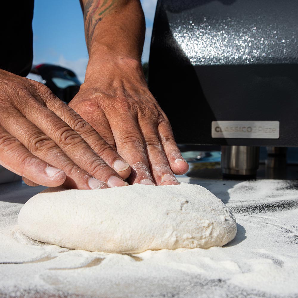 Hands placing dough onto the baking deck of an Alfa countertop gas pizza oven