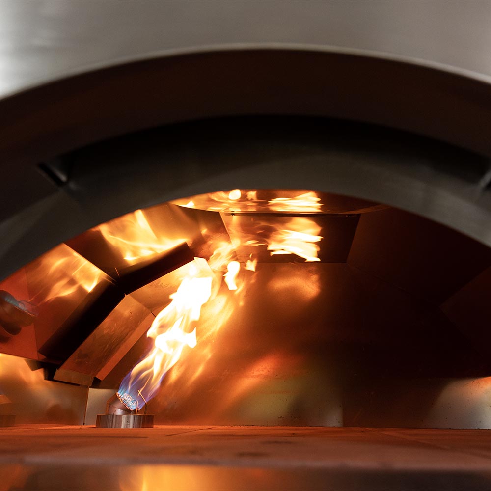 Wood-fired pizza oven interior with glowing flames over baking surface