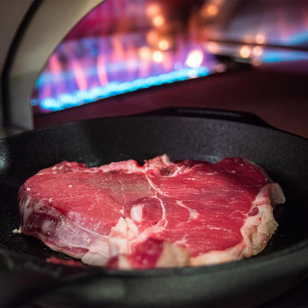 Gas pizza oven cooking surface with a steak cooking inside the heated chamber