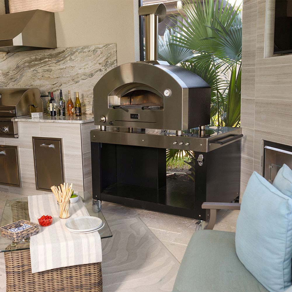 Pizza oven with stainless body and arched dome, shown outdoors on a patio setup.