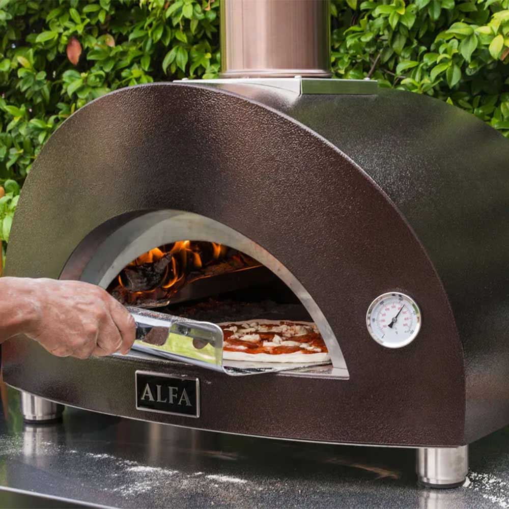Hand sliding pizza in pizza oven, with glowing flames visible in the chamber