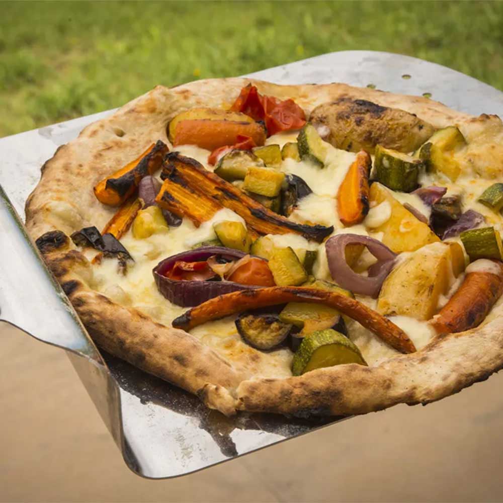 Vegetable-topped pizza on metal peel with browned crust and assorted toppings
