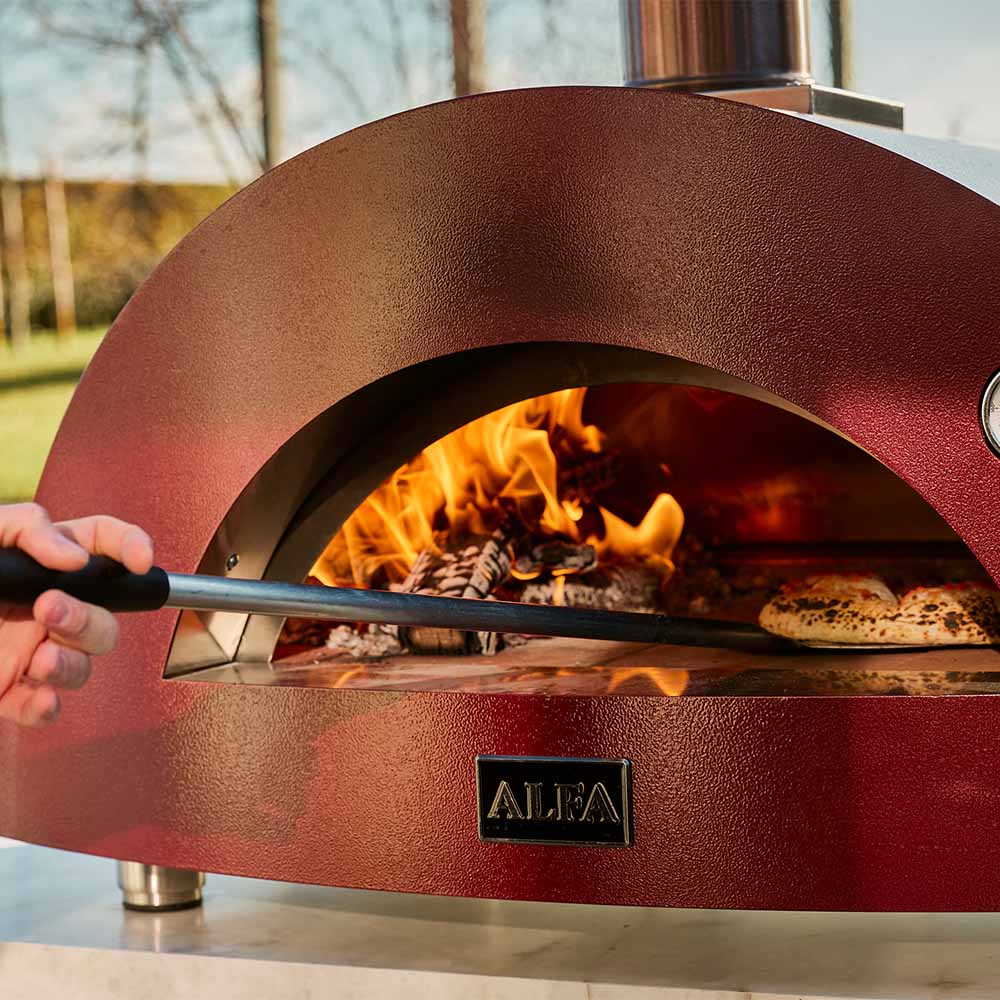 Red wood-fired pizza oven baking chamber with flames and pizza being served with peel