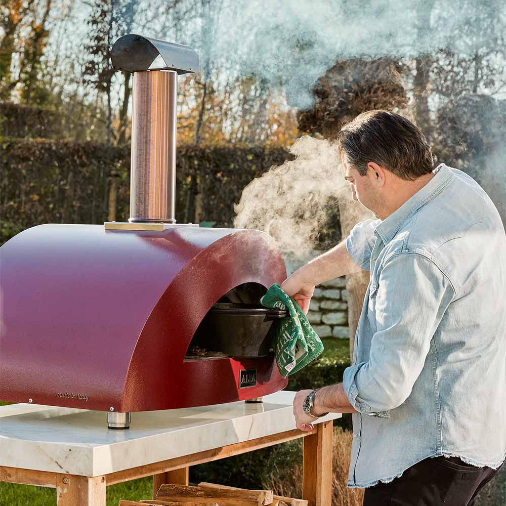 Wood-fired pizza oven in antique red with open front and cooking flames