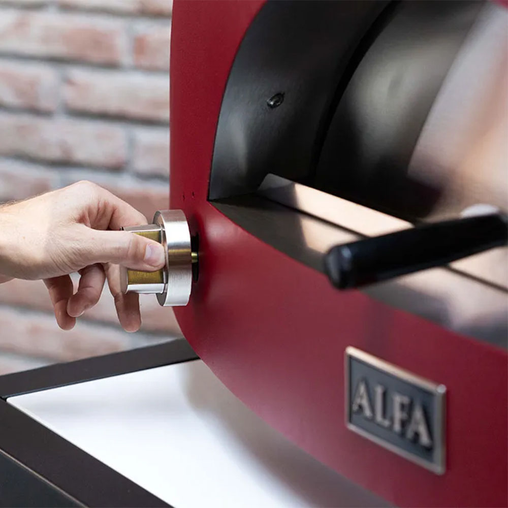 Red pizza oven side with hand turning a control knob near the cooking chamber