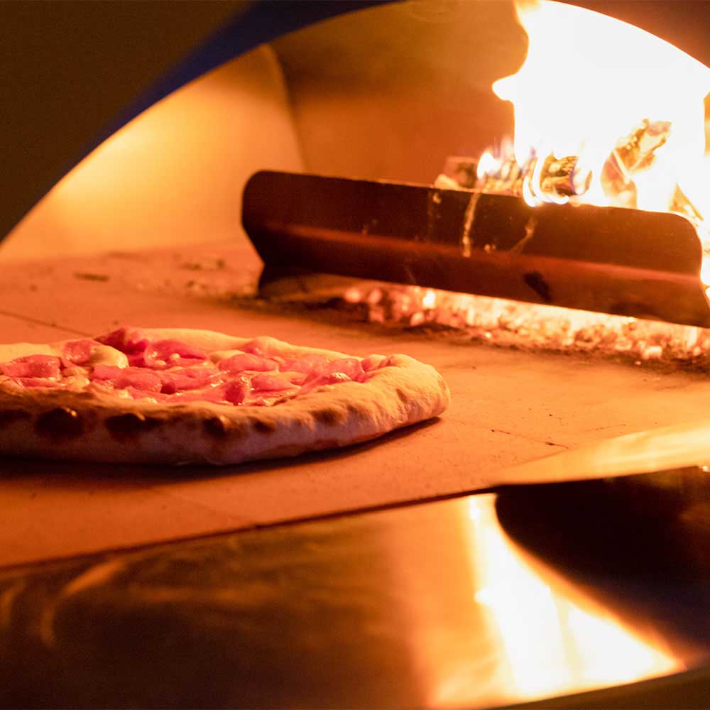 Pizza on the oven stone with visible flames inside the freestanding gas pizza oven