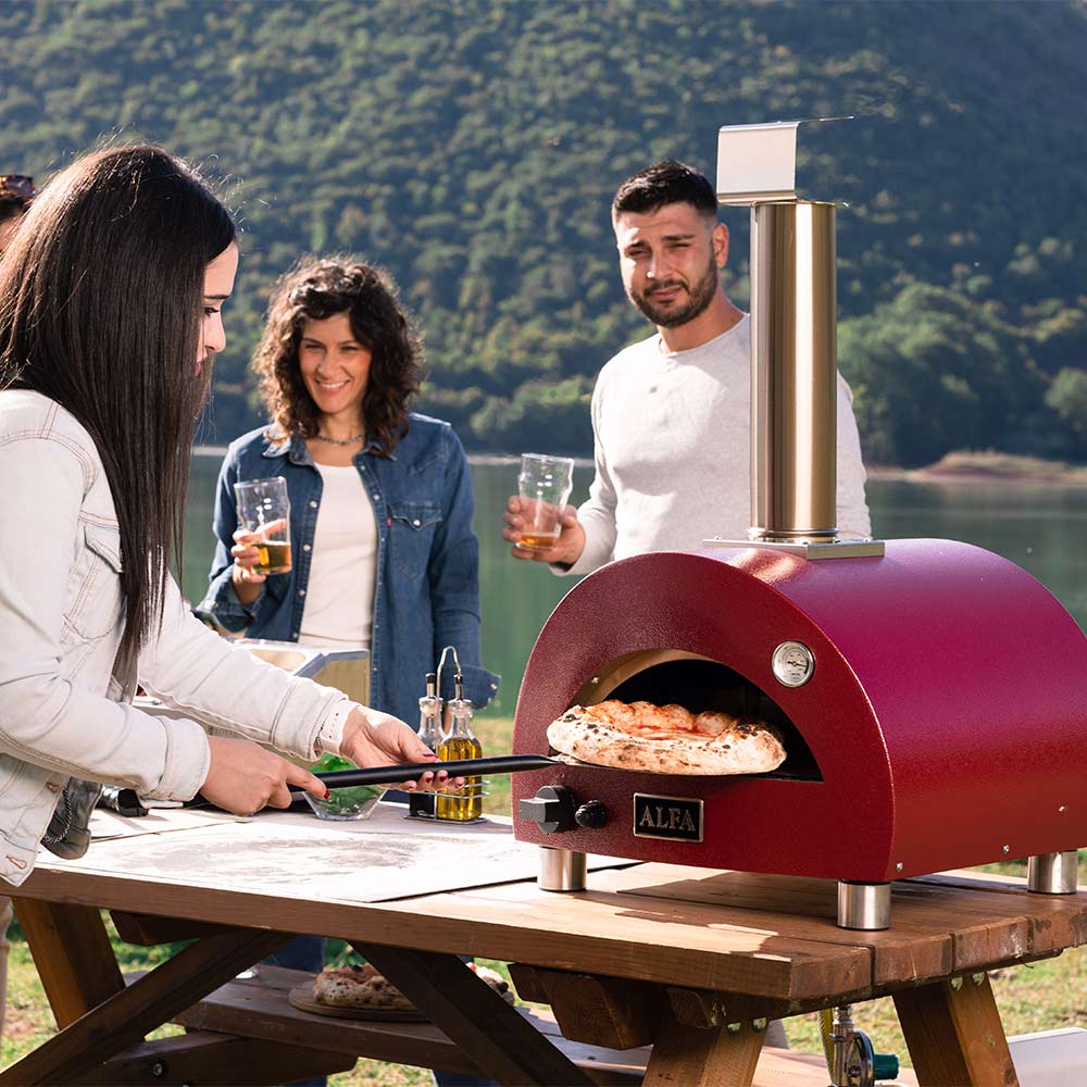 Red portable gas pizza oven on outdoor wooden counter, stainless chimney