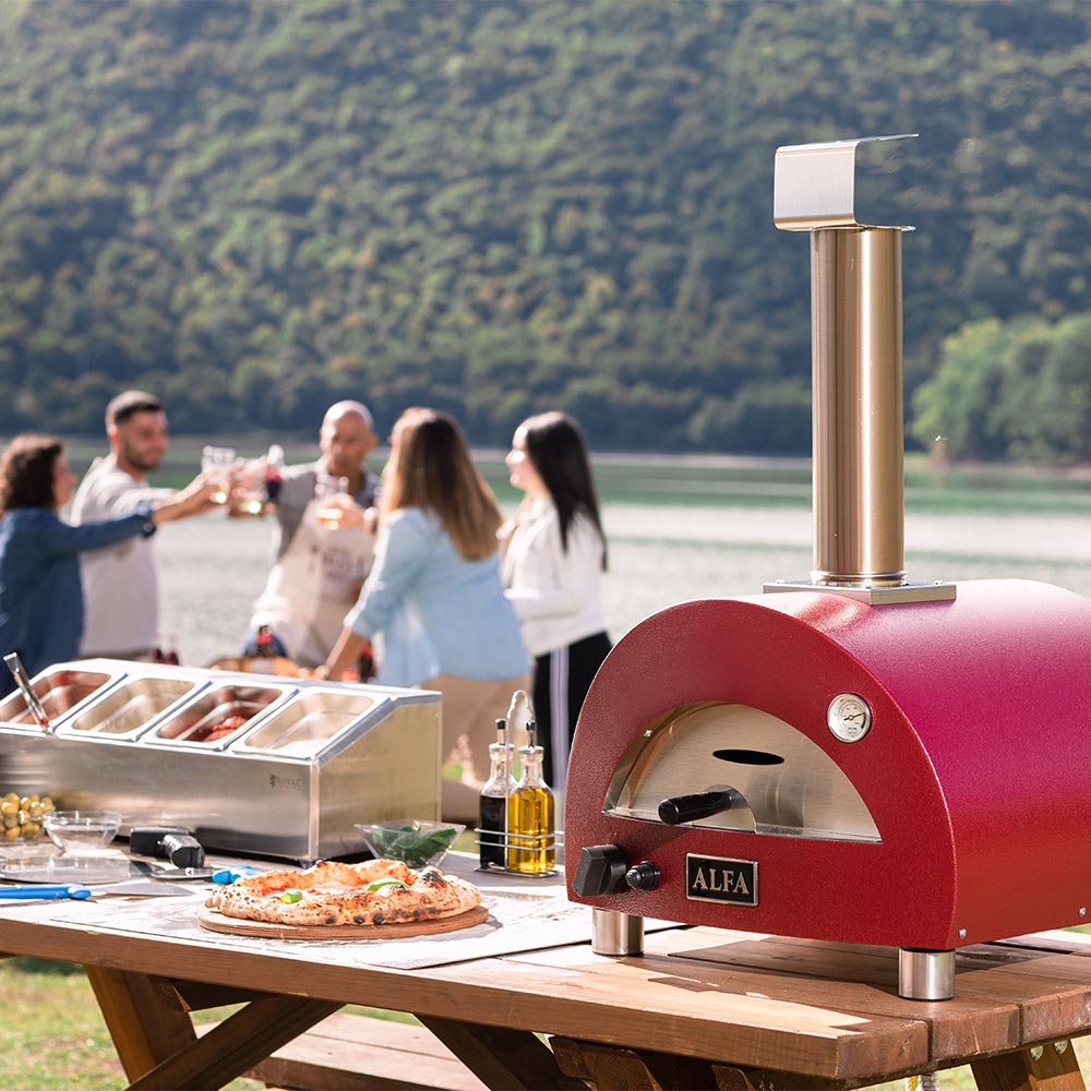 Red portable gas pizza oven on outdoor countertop with stainless chimney