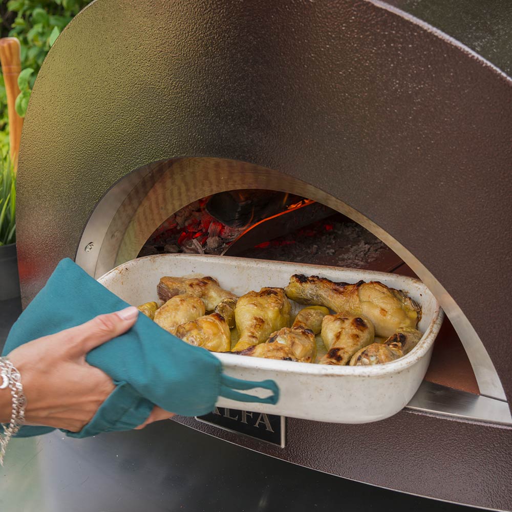 Wood-fired pizza oven with baking dish of browned chicken on the hearth