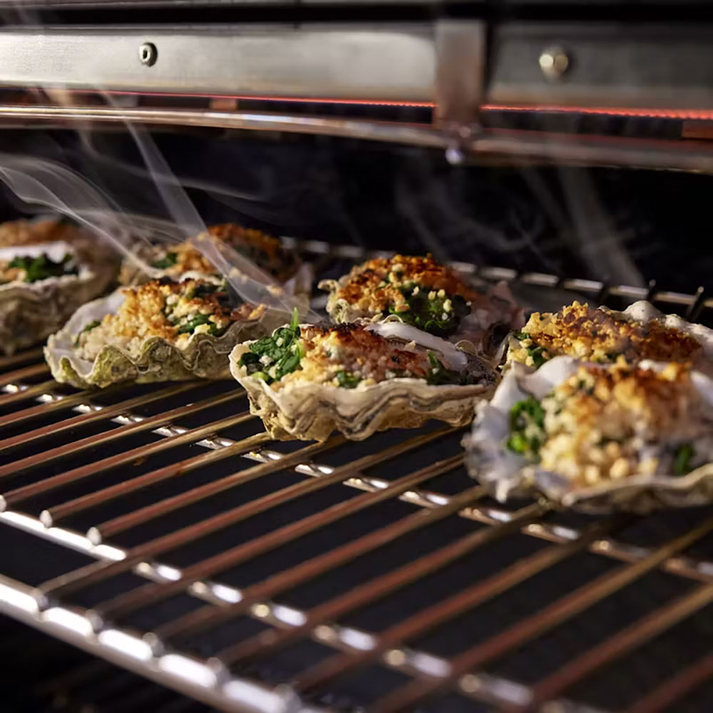 Grill with multiple stuffed meat portions on metal racks, smoke rising
