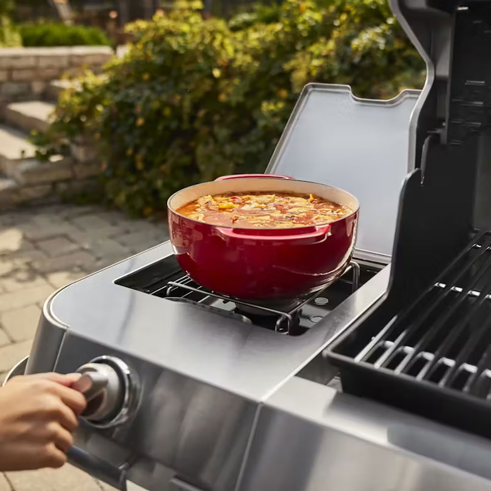 Grill with side burner skillet heating food, visible smoke
