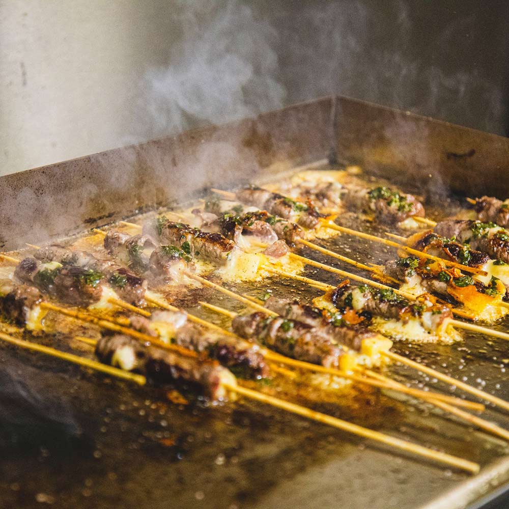 Flat-top gas griddle grilling skewers with smoke and browned food