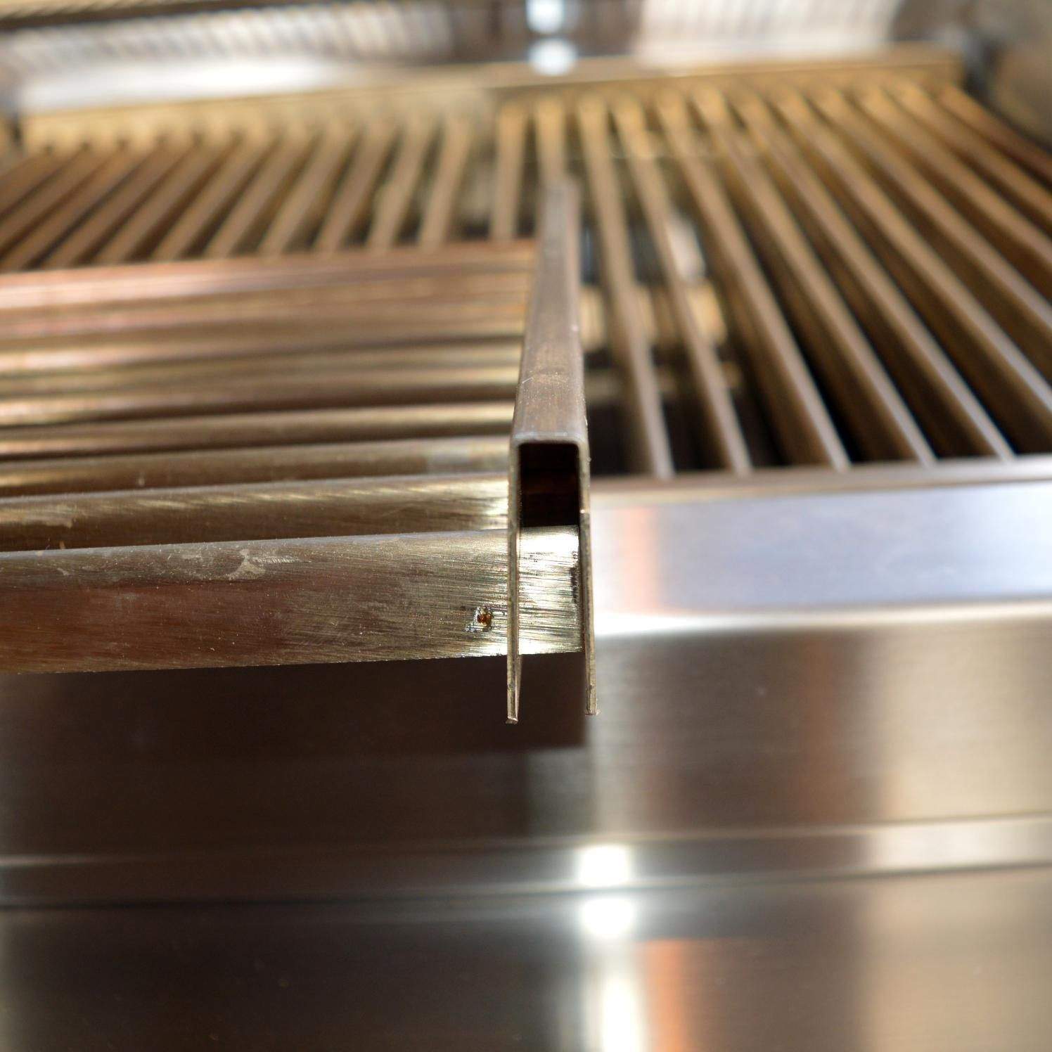 Stainless burner rail and igniter near grill grate, close-up detail