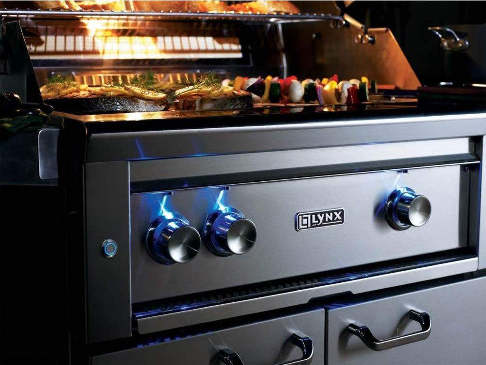 Gas grill control panel with four knobs and blue flames over stainless cooking grates
