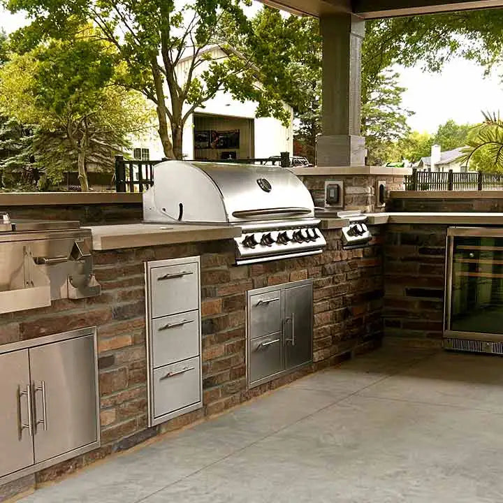 Outdoor kitchen with grill, refrigerators, and cabinets in a covered patio setting.