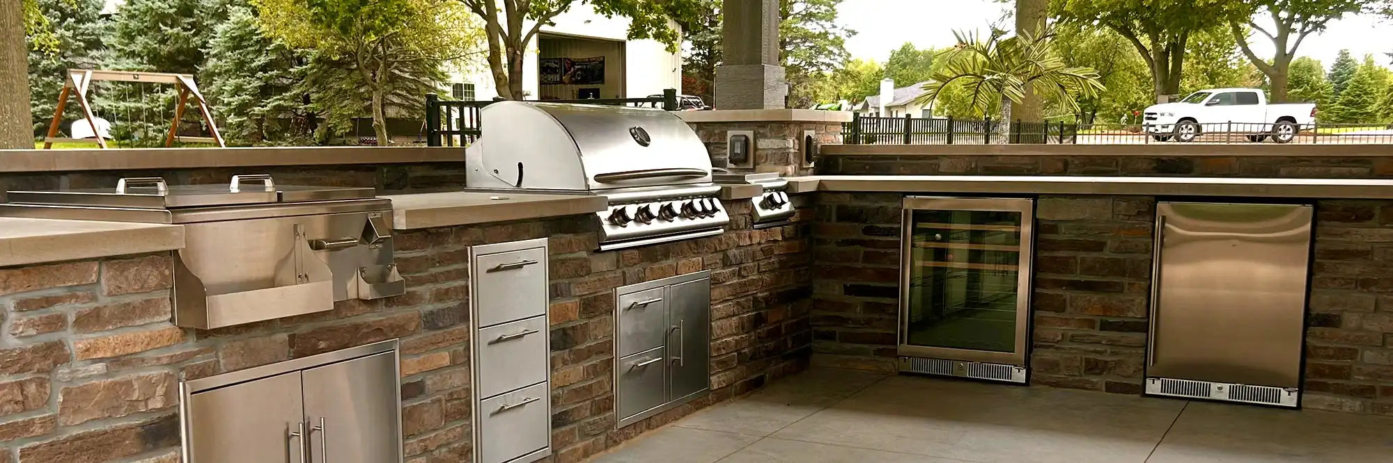 Outdoor kitchen with grill, refrigerators, and cabinets in a covered patio setting.