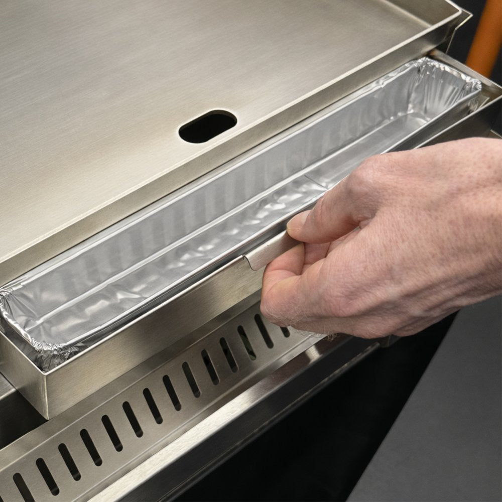 Aluminum grease tray liner being inserted into a griddle grease tray, silver foil sheet